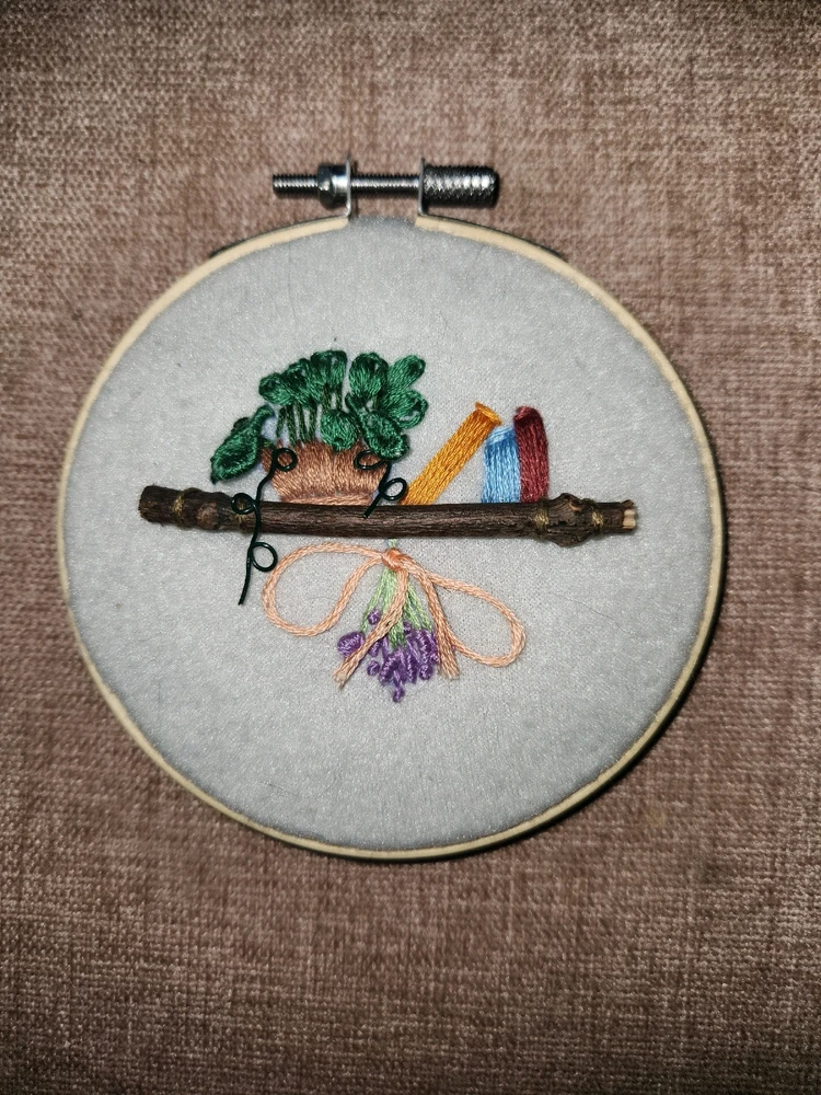 Small stick embroidered onto a hoop to be used as a shelf for a potted plant and books. Dried herbs hang from the shelf.