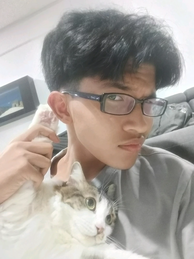 A boy in glasses holding a cat's paw to his ear kinda like a "I can't hear you" gesture