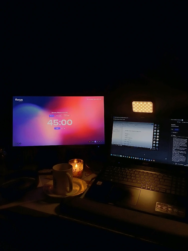 An open laptop screen and monitor showing a tomorrow timer set. A dark space with a candle lit and a soft light