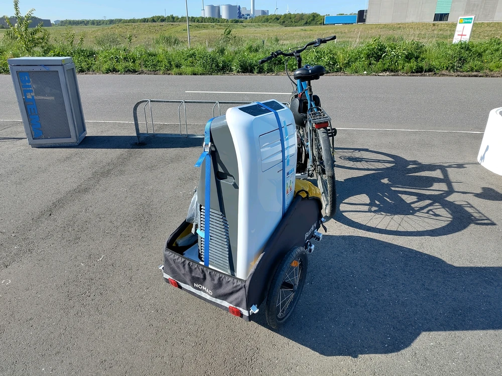 A bike with a trailer behind it and the contents of the large package safely attached to the trailer.