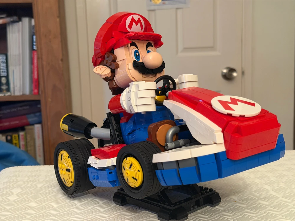 LEGO Mario races in a detailed Mario Kart, mounted on a display stand with yellow wheels and iconic red colours.