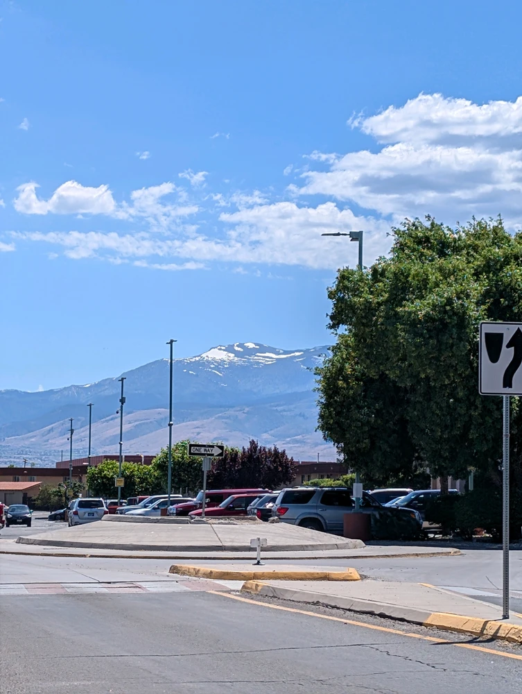 Hot day with snow capped mountains, cloudy blue skies and green trees