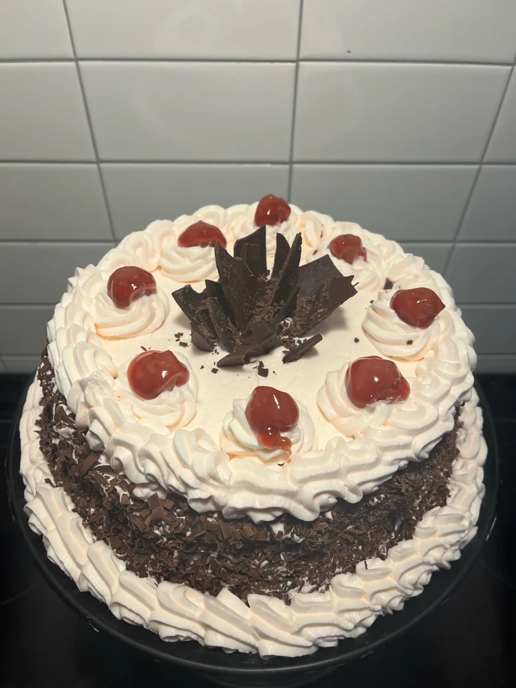 Chocolate cake with a very light pink frosting, decorated with chocolate shavings and cherries