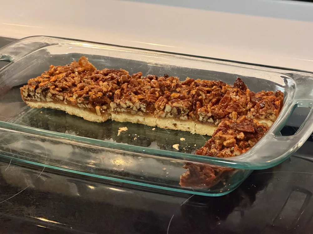 A glass baking pan partially filled with pecan pie bars