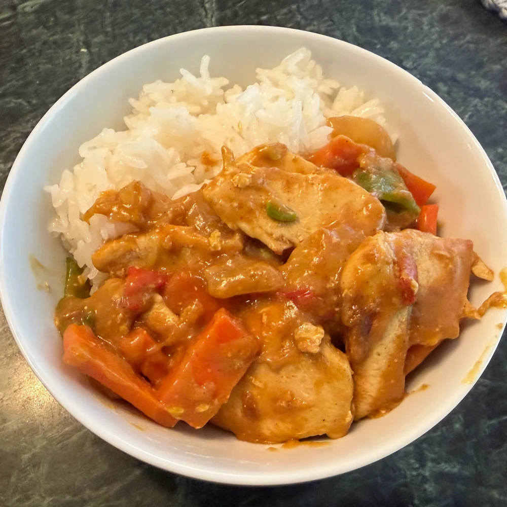 Bowl of chicken breast curry with carrots, onions, sugar snap peas, and peppers.