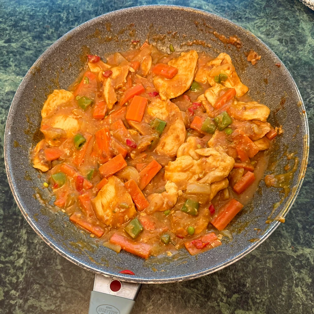 Frying pan with chicken breast curry with carrots, onions, sugar snap peas, and peppers