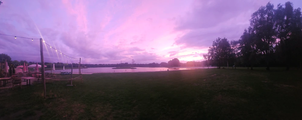 Panoramic shot of a small lake with a pink/purple sunset to the right 